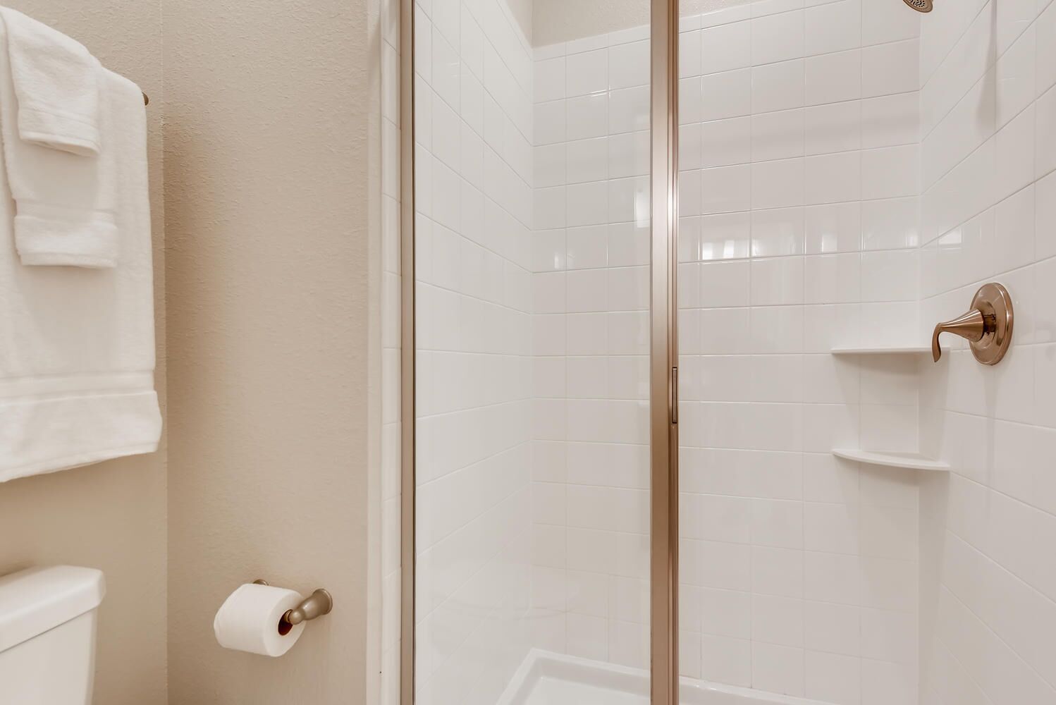 A bathroom with a glass shower door, white tiled walls, a toilet, and a towel rack.