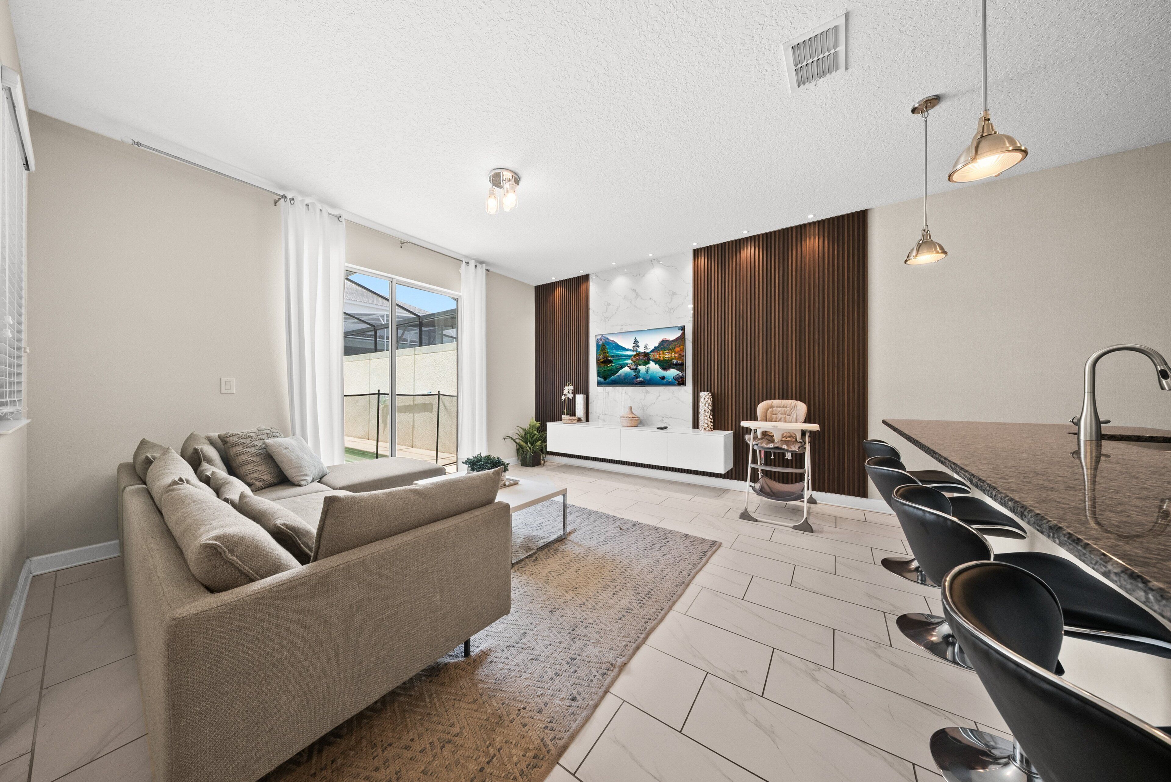 A modern living room with a sofa, a dining area with chairs, a kitchen with a sink, and a large window.
