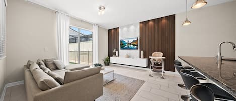 A modern living room with a sofa, a dining area with chairs, a kitchen with a sink, and a large window.