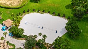 An aerial view of a beach with a volleyball net, palm trees, and a building with a tiled roof. - 1556 PD - Poolside Bliss: Enchanted 4BR Townhome (Four Corners)