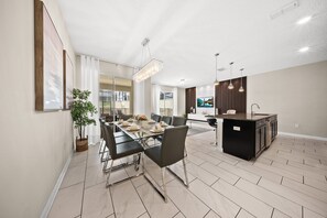 A modern kitchen with a central island, a dining area with a glass table, and a living space with a large window.