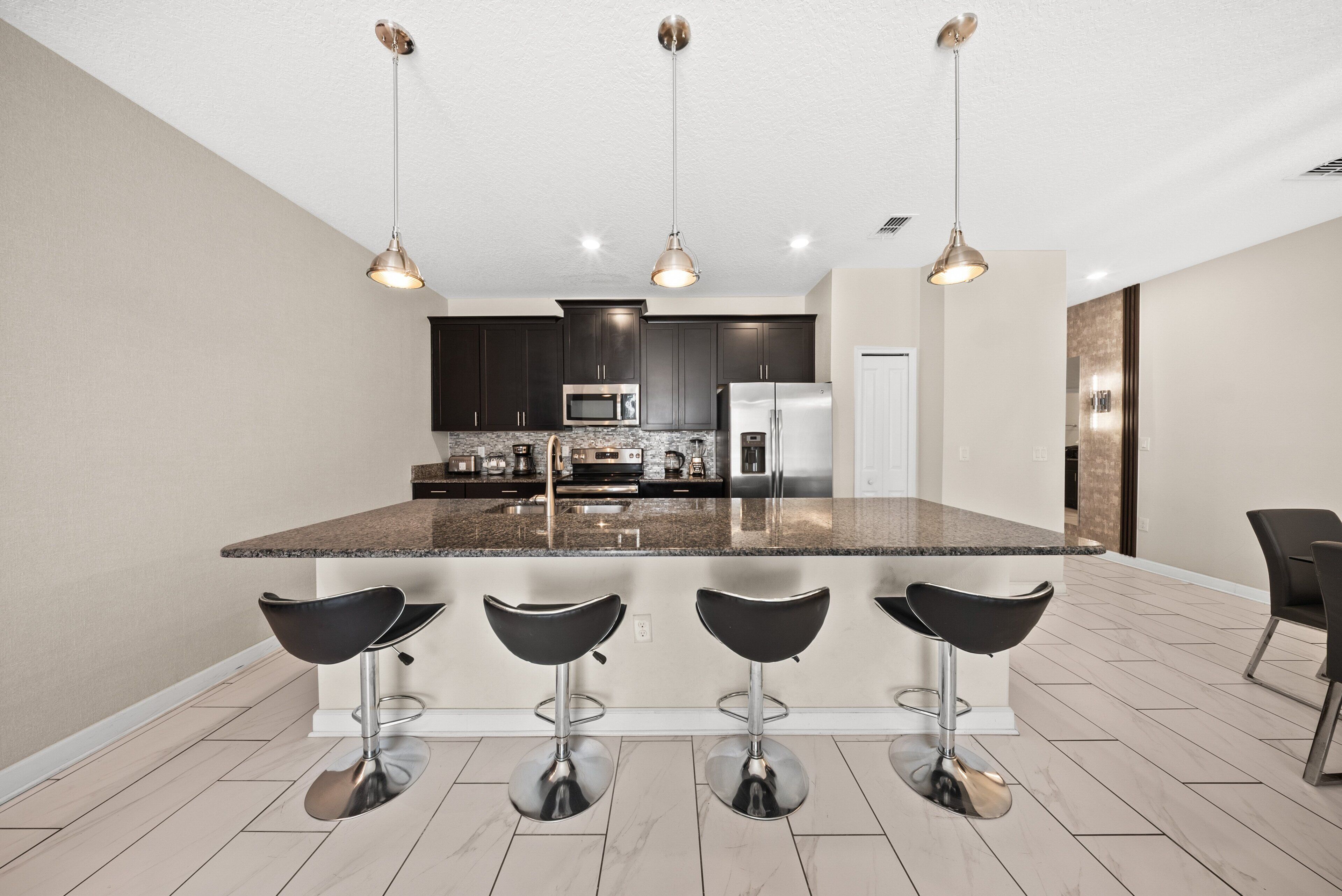 Een moderne keuken met donkere kastjes, roestvrijstalen apparatuur en een centraal eiland met barstoelen.