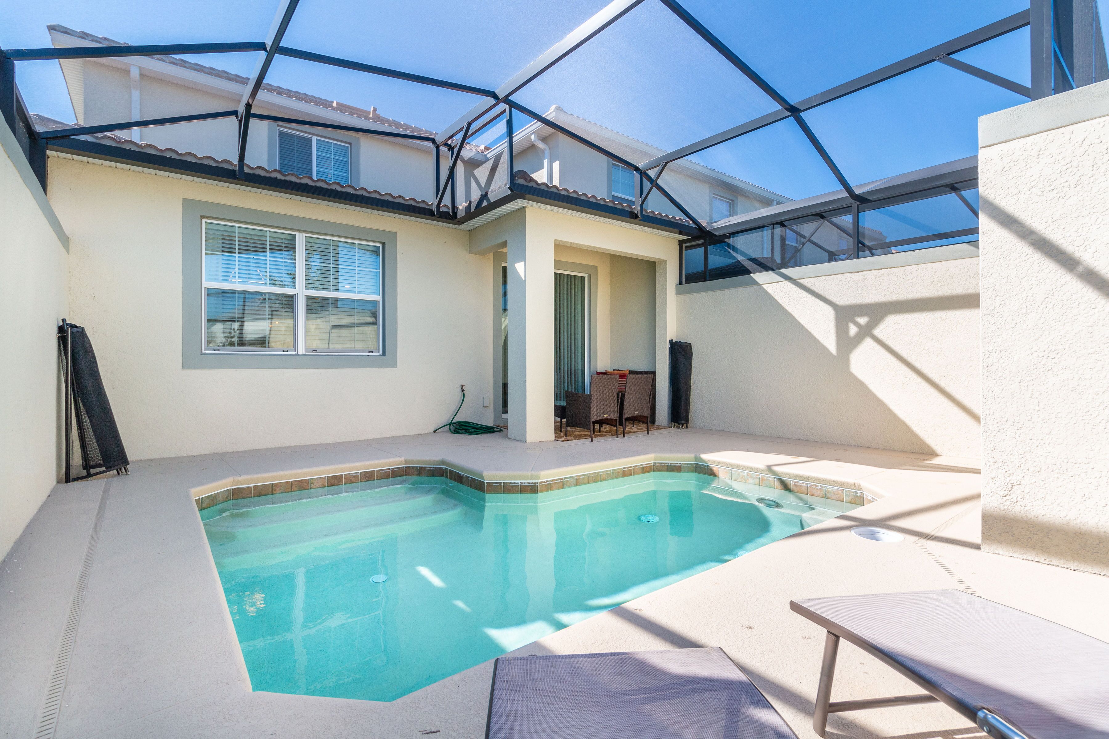 A swimming pool with a glass ceiling, a patio area with a table and chairs, and a door leading to another room.