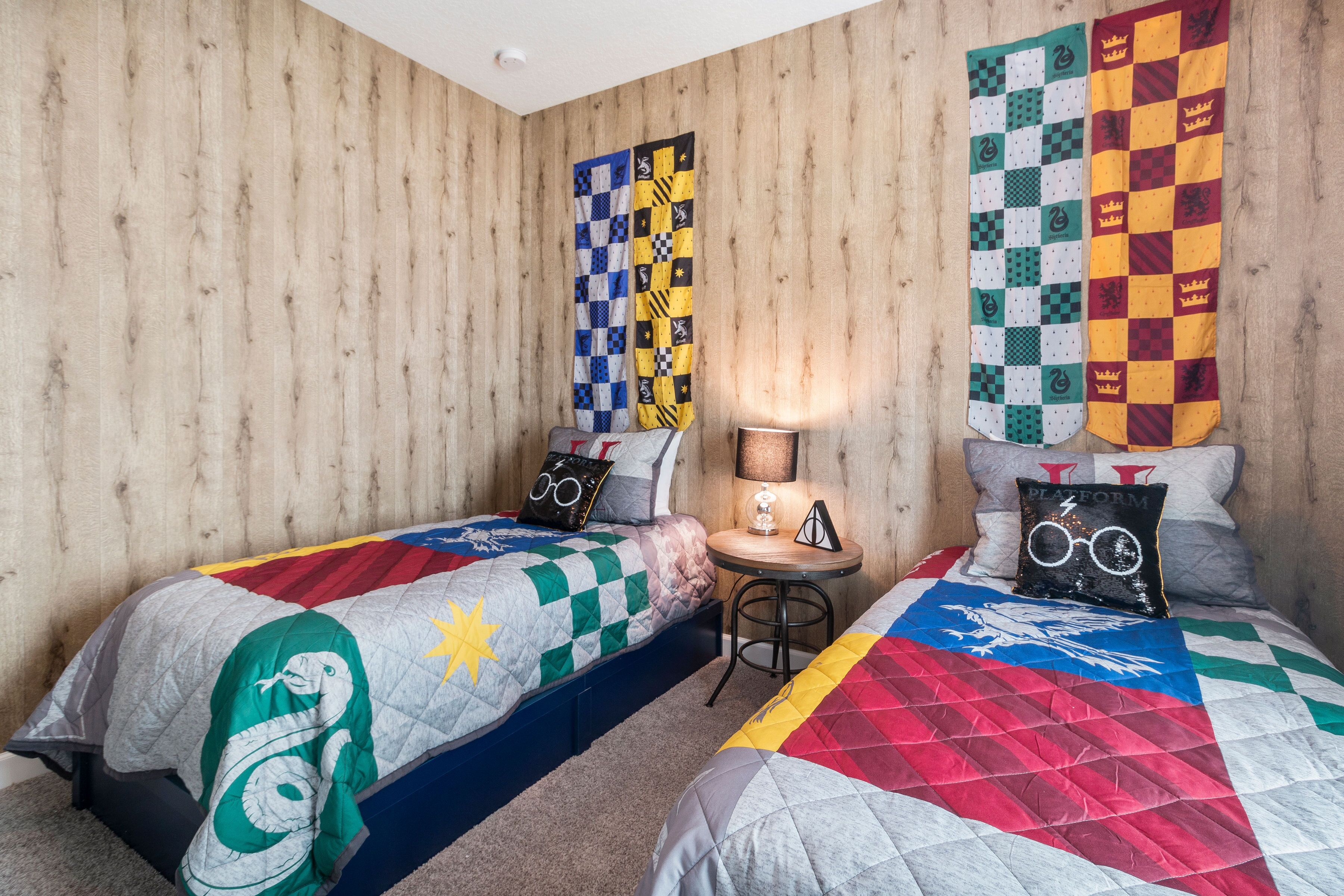 A room with two beds, each with a distinct quilt. There is a small table with a lamp between the beds.