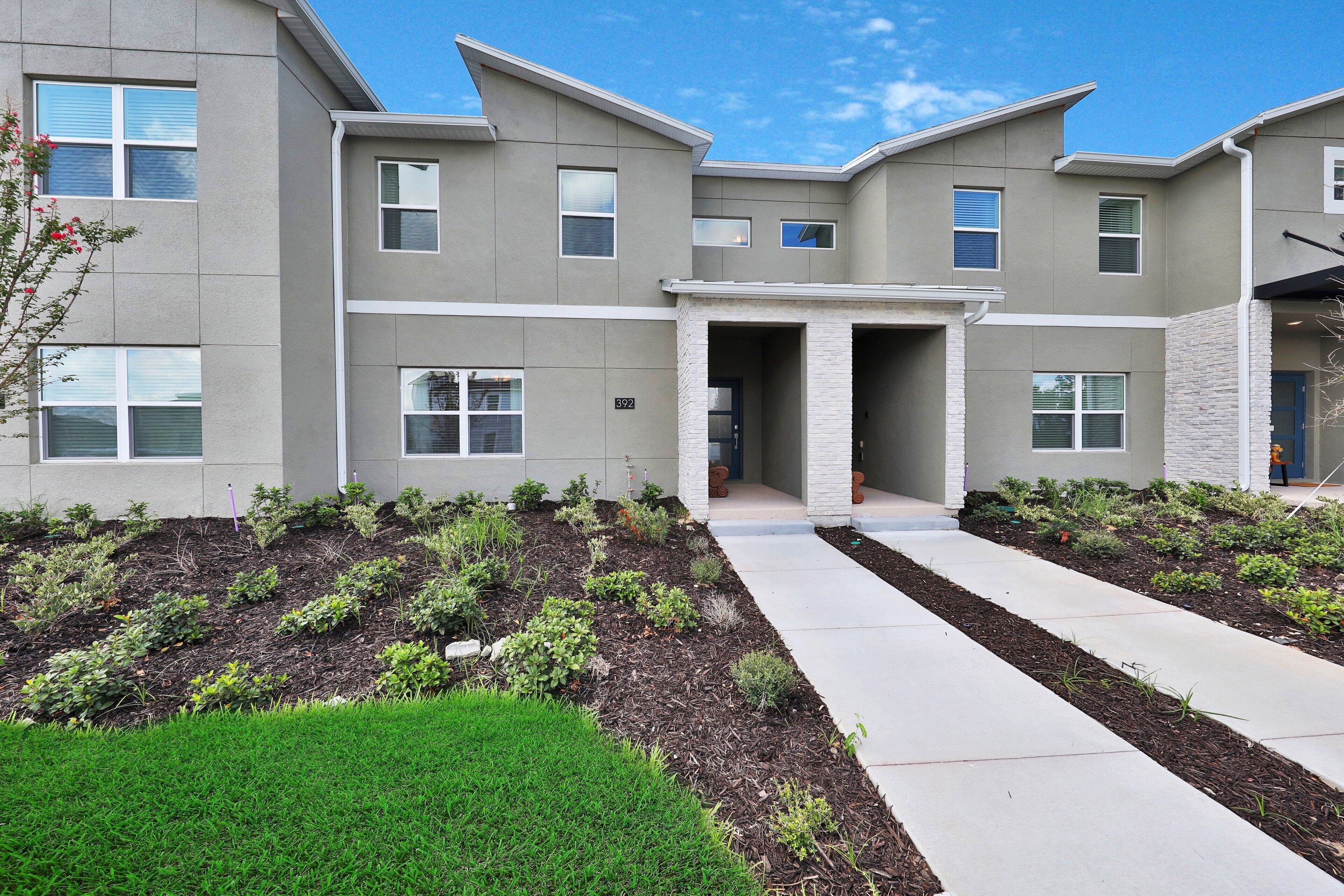 A modern multi-story residential building with a landscaped front yard, a driveway, and a well-maintained lawn.