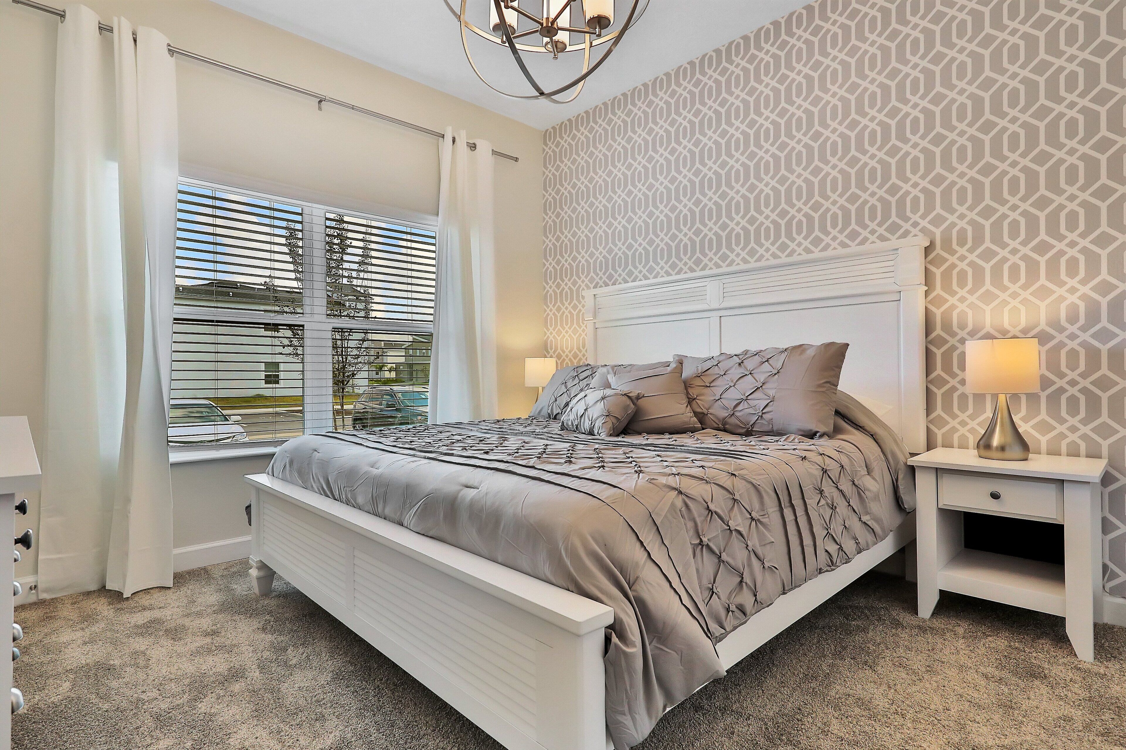 A bedroom with a bed, bedside tables, a window with curtains, and a patterned wall.
