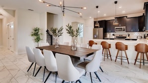 Een moderne keuken met donkere kastjes, een centraal eiland en een eetgedeelte met een houten tafel en witte stoelen.