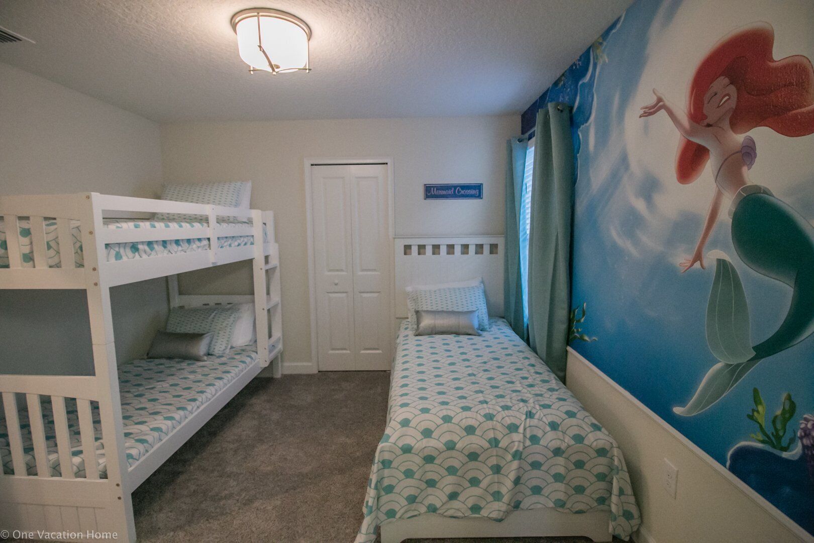 Una habitación infantil con literas, una cama individual, un mural de una sirena y un cartel que dice 'Mermaid Crossing'.
