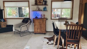 Un coin repas chaleureux avec une table en bois, des chaises, un tapis en peau de vache et un néon indiquant « Bar ».