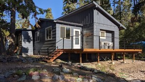 Une maison moderne à deux étages, dotée d’une terrasse en bois et d’un chemin en pierre menant à l’entrée.