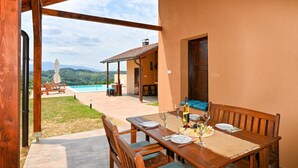 A wooden dining table set for two with a view of a swimming pool and mountains in the background. - Awesome home in Beretinec with sauna (Beretinec)
