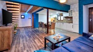 A modern living room with a sofa, a coffee table, and a TV. There is a dining area with chairs and a table. The kitchen is visible in the background with cabinets and a countertop. - Awesome home in Beretinec with sauna (Beretinec)