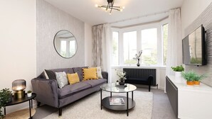 A modern living room with a grey sofa, a round coffee table, a round mirror, and a large window with curtains. - Splendid Apartment near City Centre (Edinburgh)