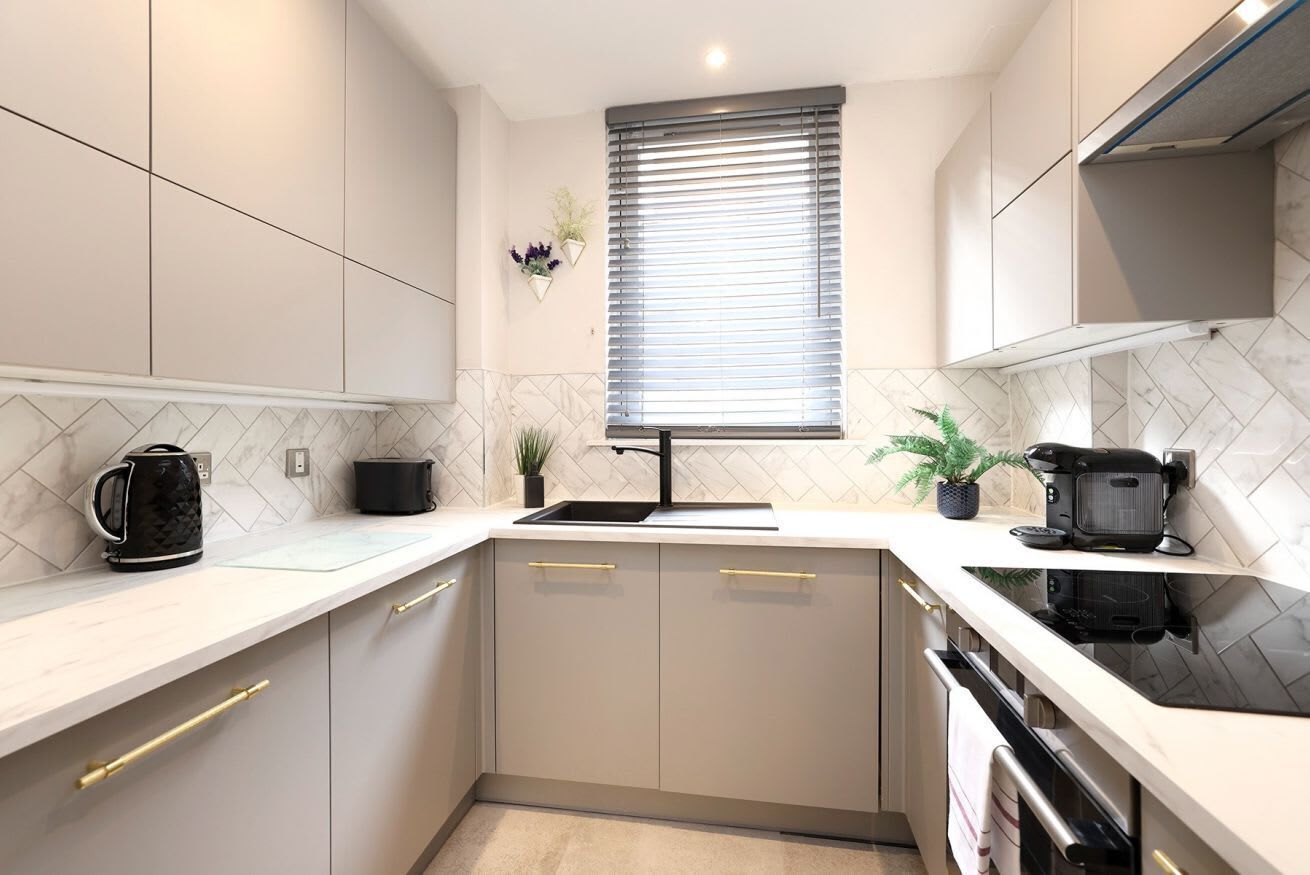 A modern kitchen with white cabinetry, a black stove, and a window with blinds.