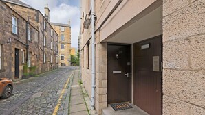 A narrow cobblestone street with a parked car and a building entrance with a dark door and a small window. - Splendid Apartment near City Centre (Edinburgh)