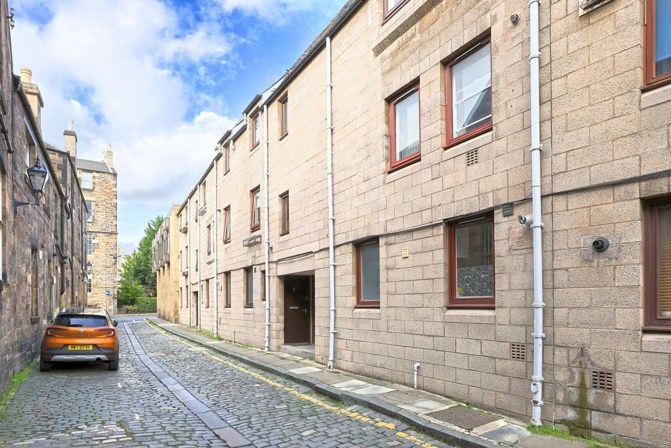 Une ruelle étroite pavée, bordée de bâtiments traditionnels en briques, avec une voiture garée et un ciel dégagé.