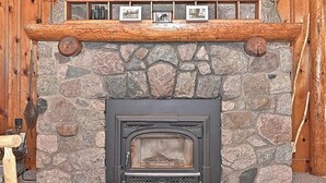 A stone fireplace with a wooden mantel, a fish decoration, and framed pictures. - Chapel Hill Resort (Spring Lake)