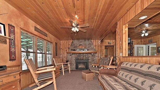 A cozy log cabin interior with a stone fireplace, wooden furniture, and a ceiling fan. - Chapel Hill Resort (Spring Lake)