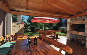 An outdoor patio with a wooden table, benches, and a barbecue grill.