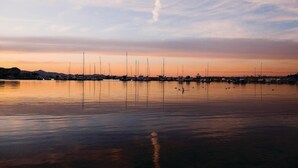 Un puerto deportivo con varios veleros amarrados, agua tranquila y una costa distante con edificios.