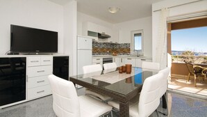 Una cocina moderna con armarios blancos, un refrigerador negro y un protector contra salpicaduras de azulejos. Hay una zona de comedor con una mesa de vidrio y sillas blancas.