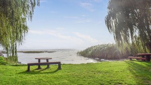 Et picnicområde med bænke og et bord ved et roligt vandareal, omgivet af frodig vegetation.