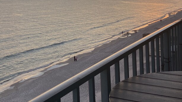 A beach view with a wooden deck and railing, overlooking the ocean and a sunset.