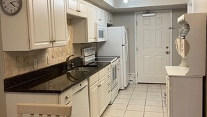 A compact kitchen with white cabinets, a microwave, a refrigerator, and a clock on the wall.