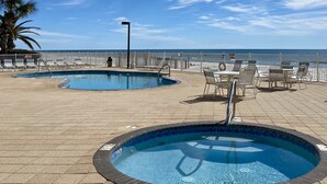 A pool area with two pools, lounge chairs, and a table with chairs.