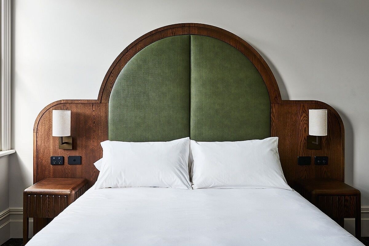 A neatly made bed with white linens, a wooden headboard with a green upholstered section, and two bedside tables with lamps.