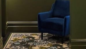 A hallway with a blue chair, a patterned rug, and a light fixture. - Portarlington Grand Hotel (Portarlington)