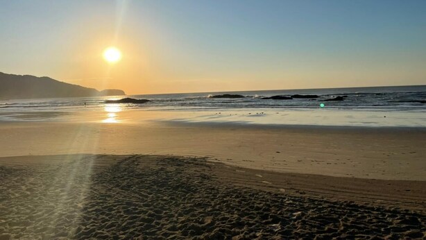 A beach with the sun setting over the ocean, creating a serene atmosphere. - Spacious, beautiful apartment - 3 blocks from the beach! (Guarujá)