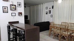 A modern living space with a dining area, a black sofa, and a TV in the background. - Spacious, beautiful apartment - 3 blocks from the beach! (Guarujá)