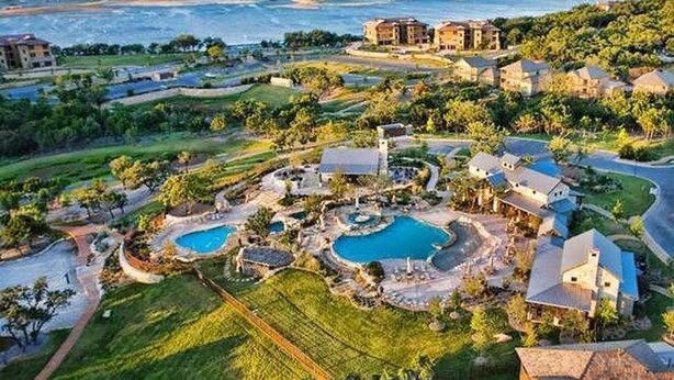 Een luchtbeeld van een resort met meerdere zwembaden, weelderige begroeiing en strandwoningen.