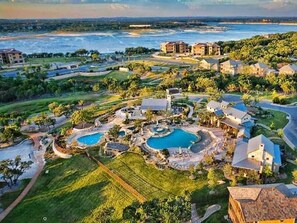 Eine Vogelperspektive auf ein Resort mit mehreren Schwimmbecken, üppiger Vegetation und Strandhäusern.