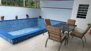 Ein Pool mit blauen Mosaikfliesen, umgeben von einer weißen Mauer mit einem Fenster und Topfpflanzen.