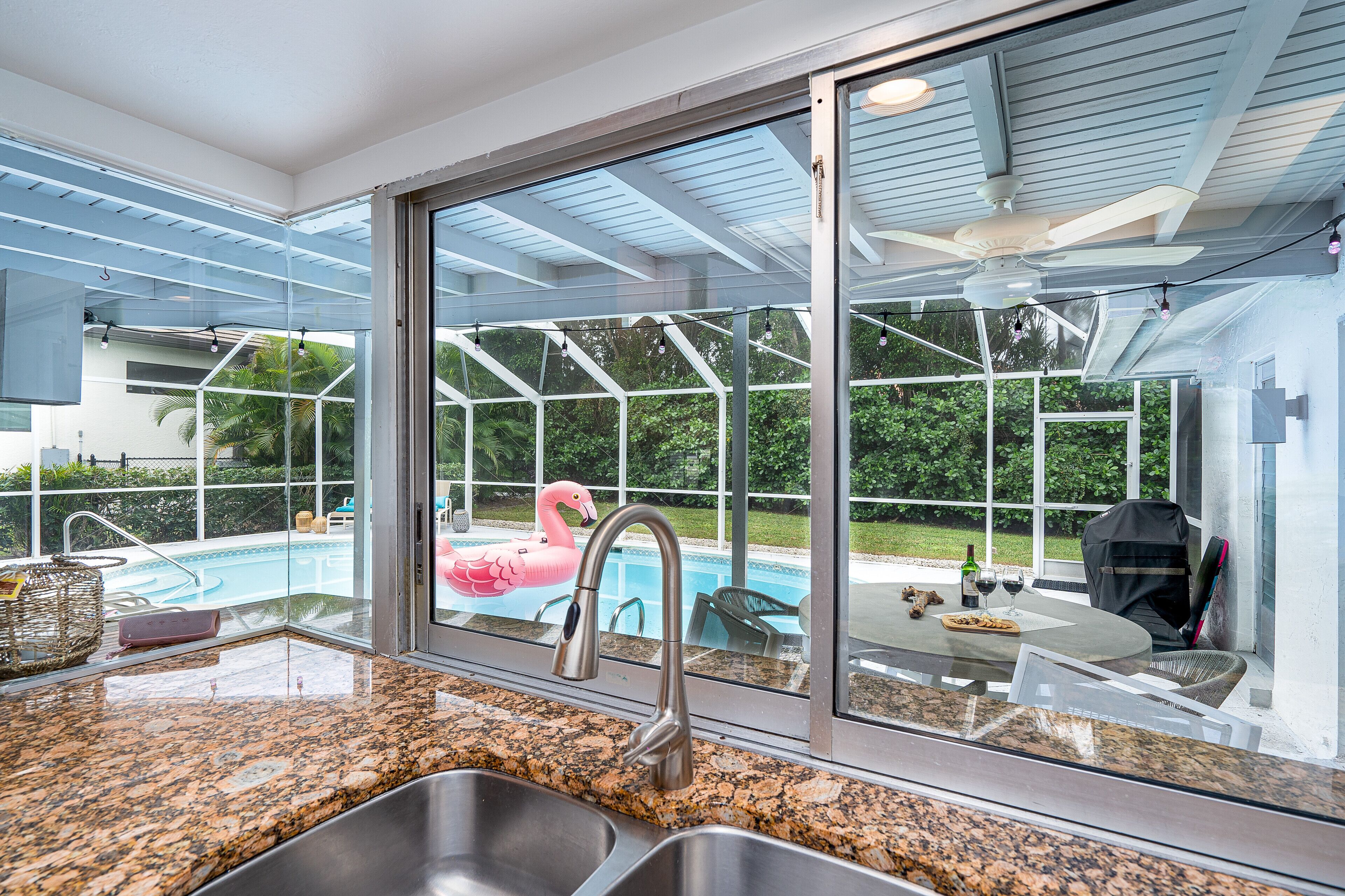 A kitchen with a large window overlooking a swimming pool, a ceiling fan, and a dining area with outdoor seating.
