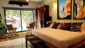A bedroom with a large bed, two wicker chairs, a wooden cabinet, and a painting on the wall. - Ekléctic Hotel Boutique (Guadalajara)