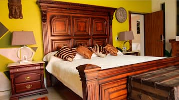 A bedroom with a wooden bed, multiple pillows, a nightstand with a lamp, a dresser, and a suitcase.