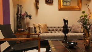 Ein Wohnzimmer mit Sofa, Couchtisch und Sessel. An den Wänden befinden sich dekorative Elemente und ein Spiegel über dem Sofa.