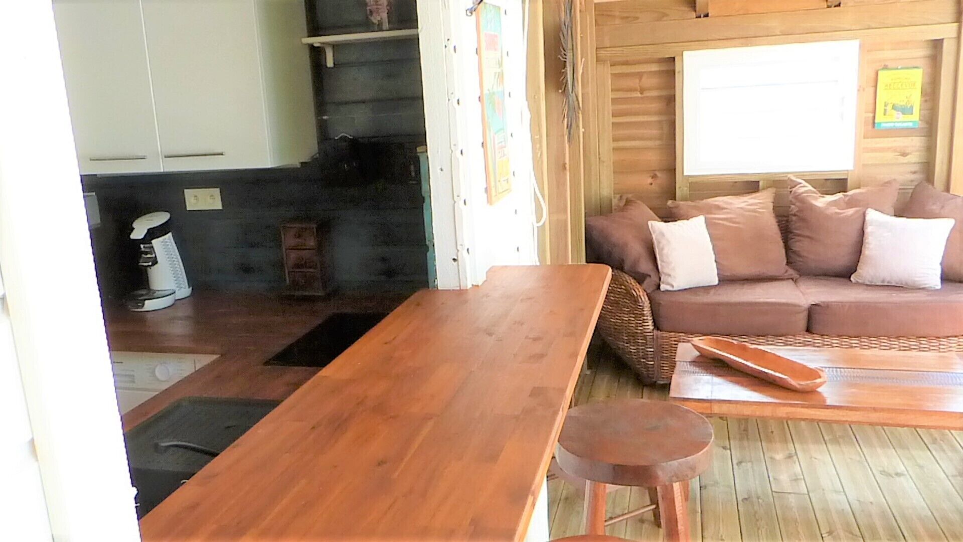 A wooden interior with a sofa, a table, and a kitchen area with cabinets and a coffee machine.