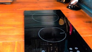 A kitchen with a black induction cooktop, wooden cabinets, and a hanging rack with bottles and utensils.