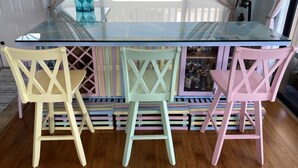 A bar area with a glass-top table, three colorful chairs, and a wooden floor. - Oceanfront Paradise w new 365' Dock Huge Tiki and Firepit.  Dogs OK (Big Pine Key)