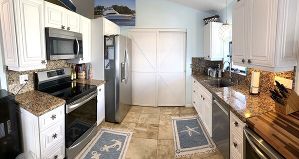 A kitchen with white cabinets, a stainless steel refrigerator, a microwave, and a granite countertop.