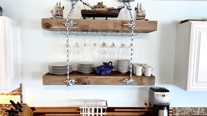 A kitchen with wooden shelves holding plates, bowls, and mugs, a coffee maker, and a hanging light fixture. - Oceanfront Paradise w new 365' Dock Huge Tiki and Firepit.  Dogs OK (Big Pine Key)