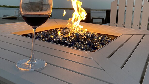 A glass of red wine on a white lounge chair with a fire feature in the background. - Oceanfront Paradise w new 365' Dock Huge Tiki and Firepit.  Dogs OK (Big Pine Key)