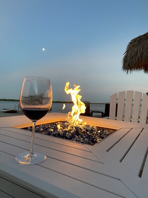 A glass of red wine on a white lounge chair with a fire feature in the background.