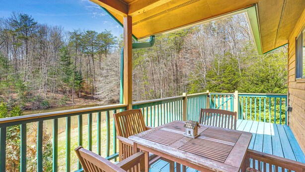 A wooden deck with a table and chairs, overlooking a forested area.