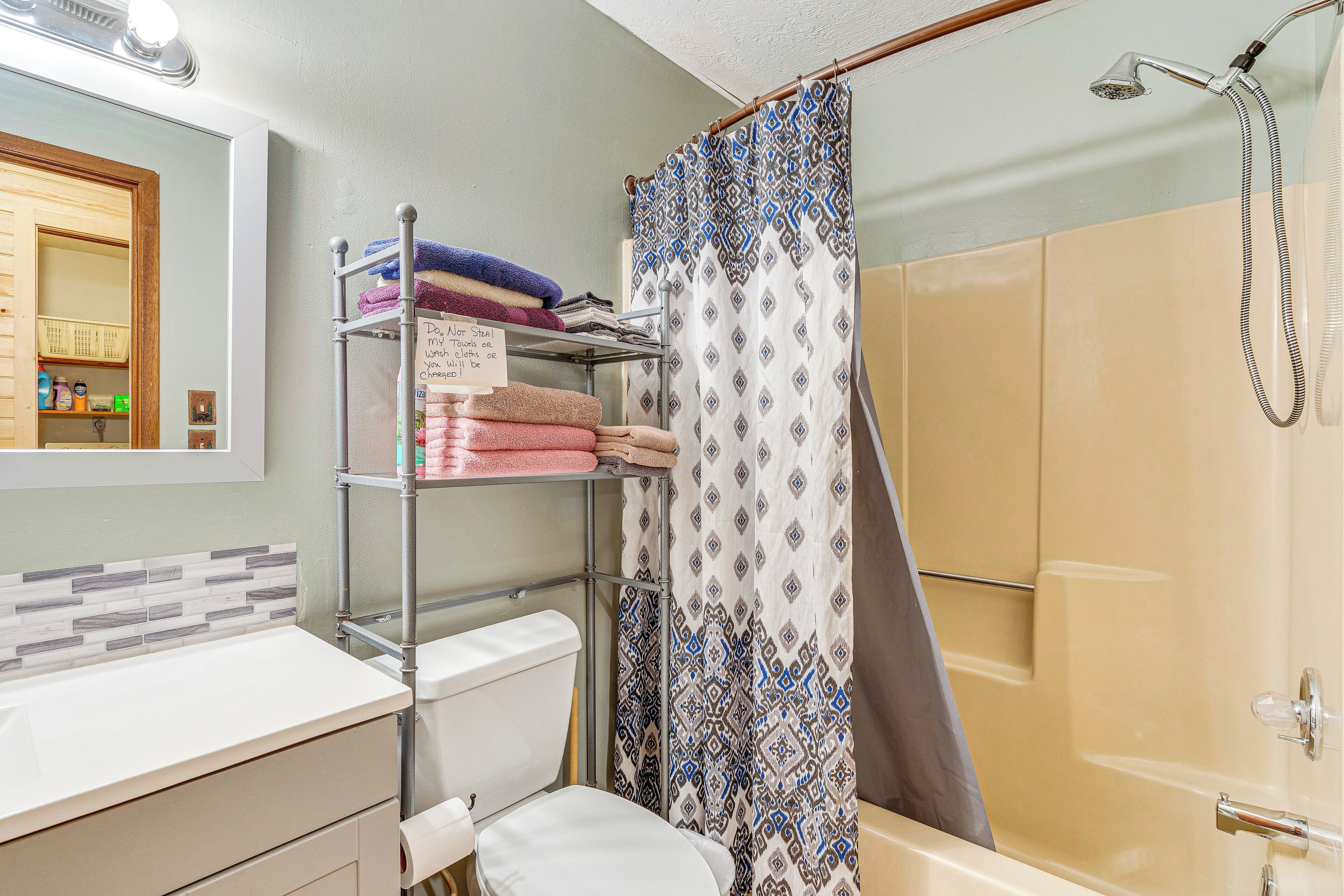 A bathroom with a toilet, sink, shower, and a towel rack with folded towels.