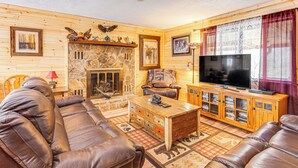 A cozy living room with a stone fireplace, leather sofas, a wooden coffee table, and a television on a wooden cabinet.